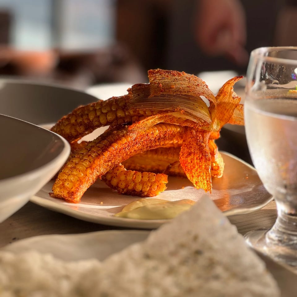 Seasoned fried chicken sandwich with crispy layers and dipping sauce on a restaurant plate, accompanied by water glasses.