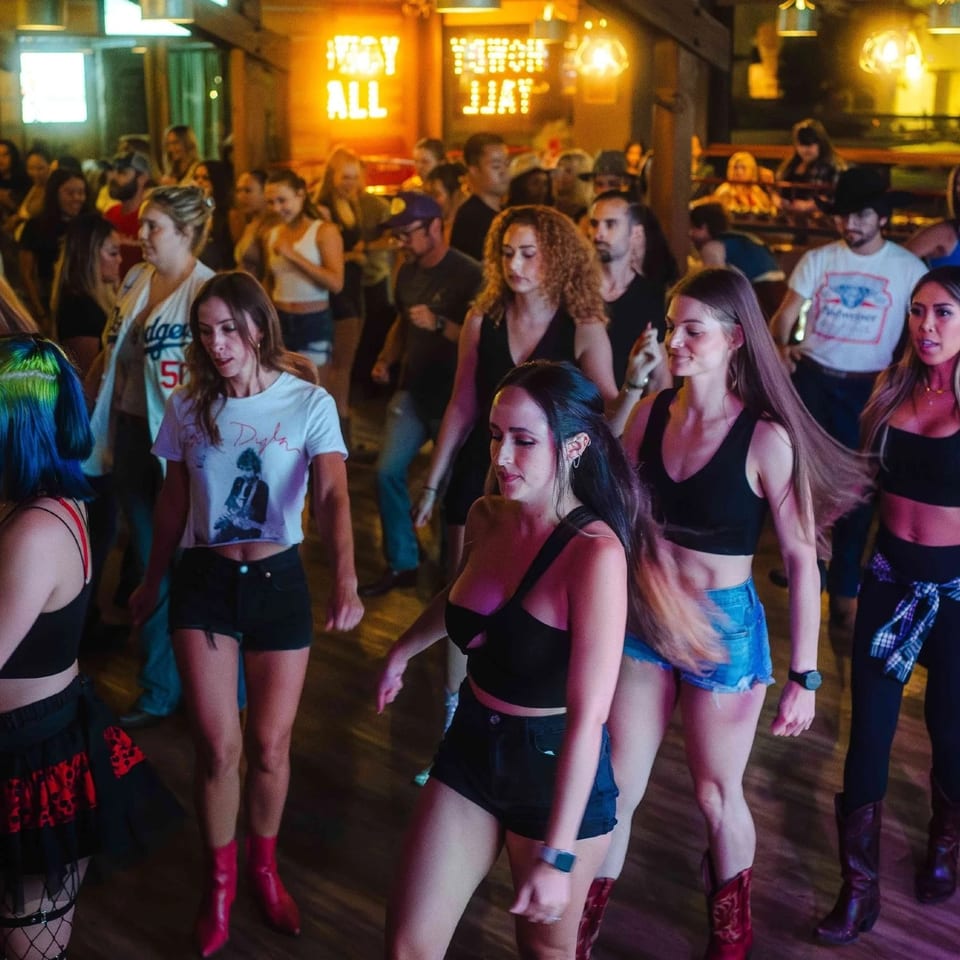 Packed crowd line dancing under the Howdy Y'all sign