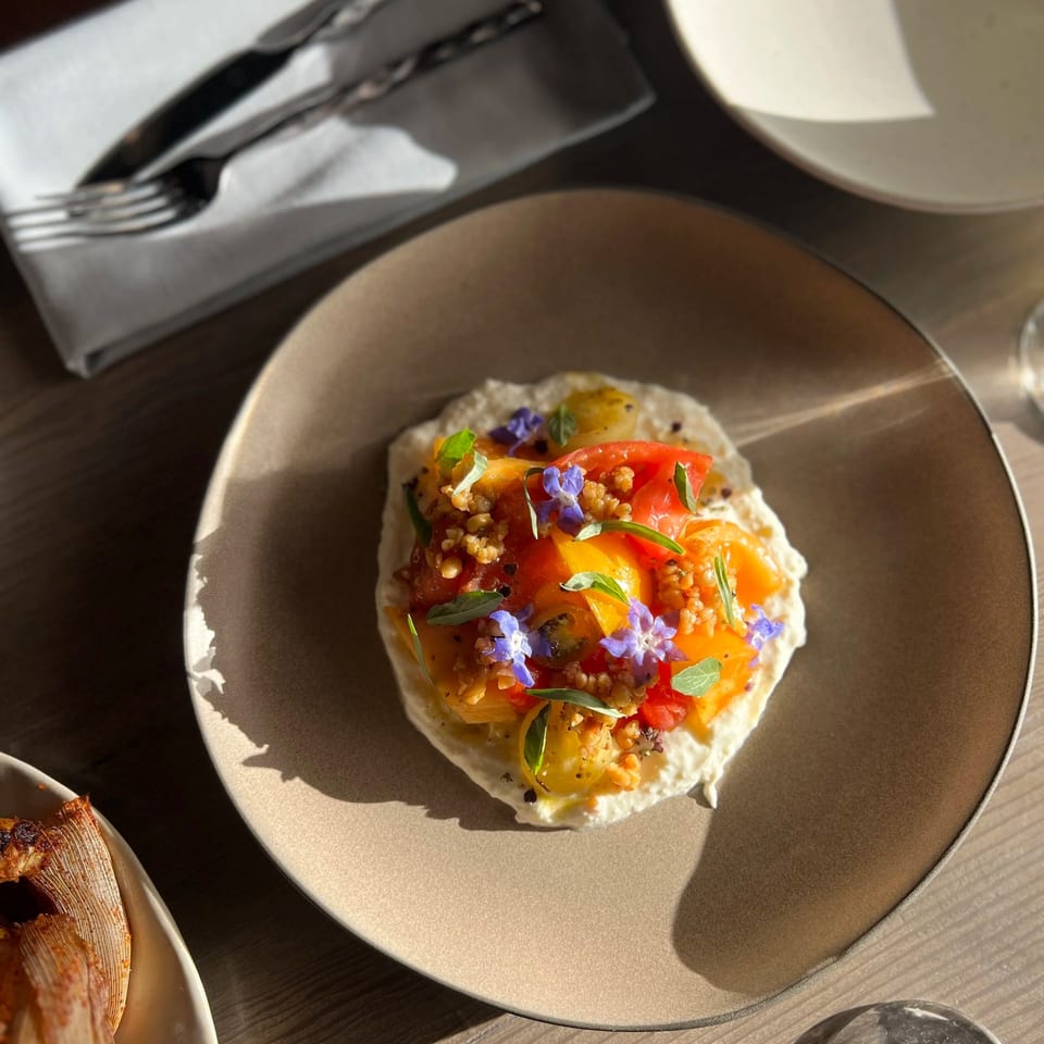 Colorful heirloom tomatoes with herbs and edible flowers served over creamy spread on a ceramic plate.